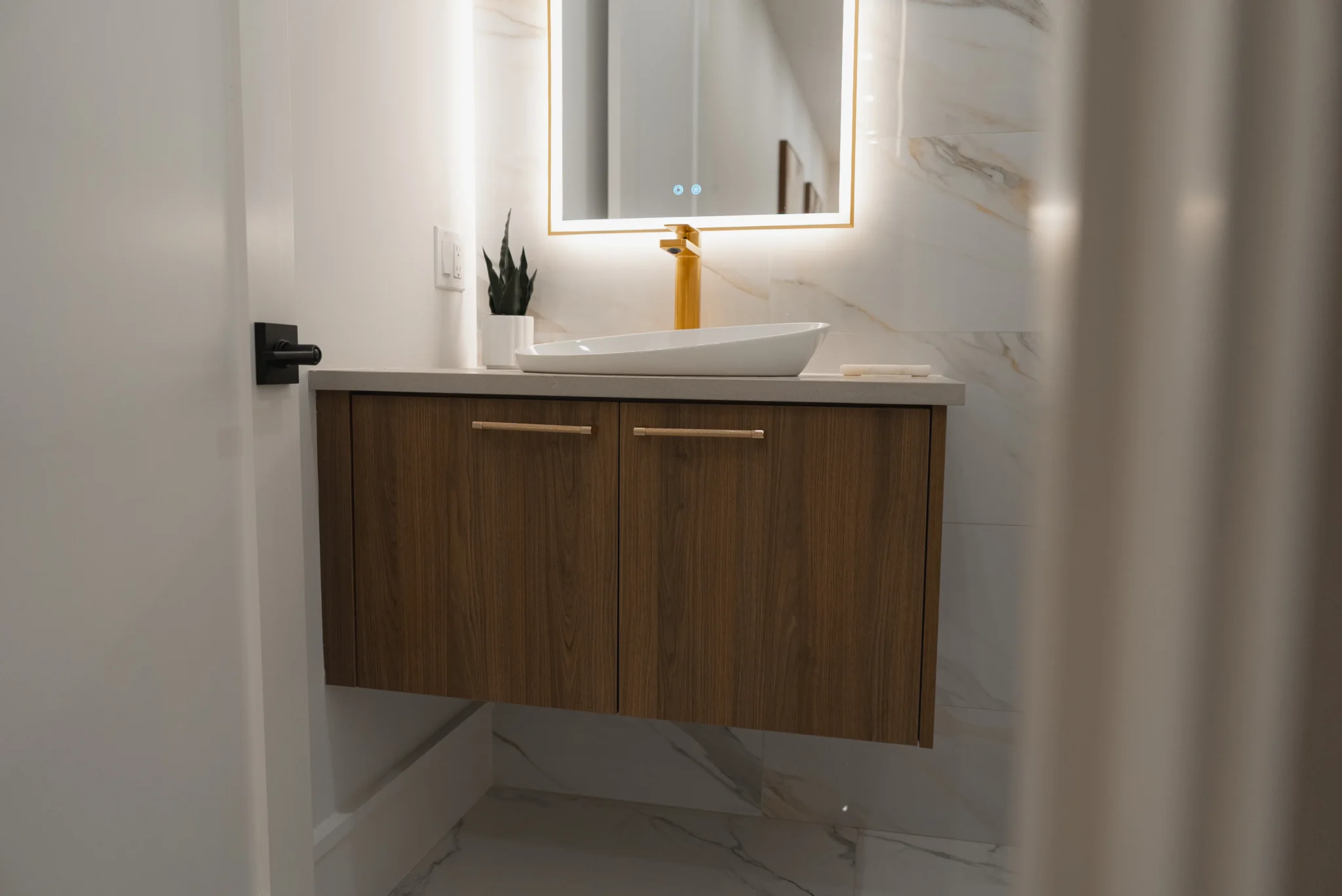 Contemporary bathroom with floating wood vanity, vessel sink, and illuminated mirror with warm accents
