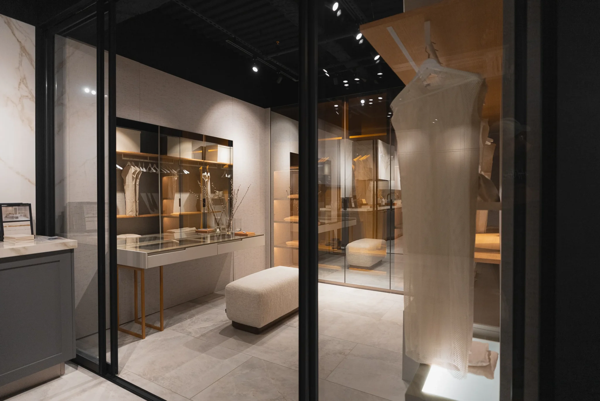 Elegant glass-enclosed dressing room with warm lighting, display shelving, and boutique-style organization