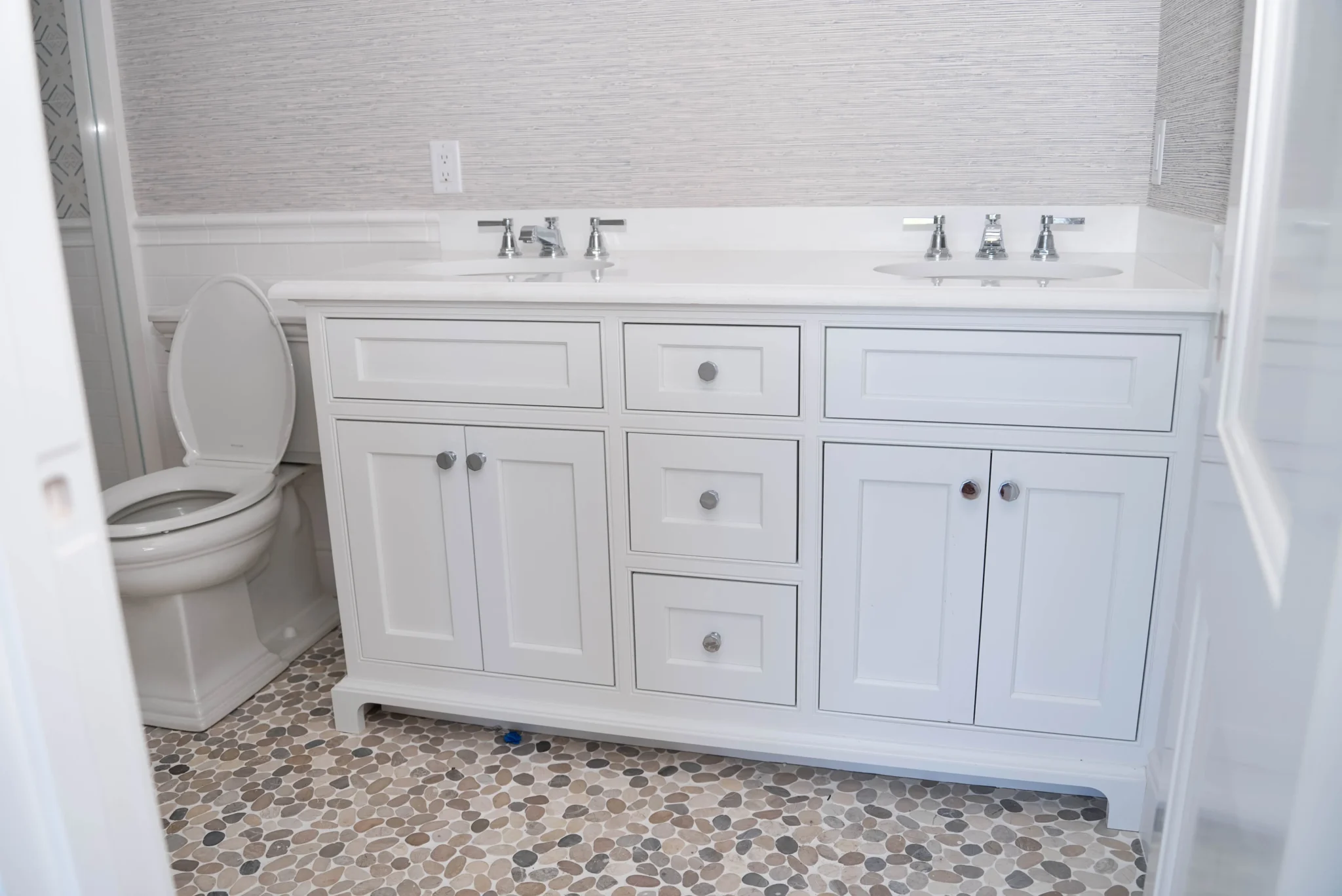 Traditional bathroom with white double vanity, shaker cabinets, and pebble stone flooring